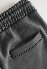 Donkergrijze joggers van zacht materiaal, met een geribde tailleband en een achterzak met een gleufopening. Soepele textuur overal.