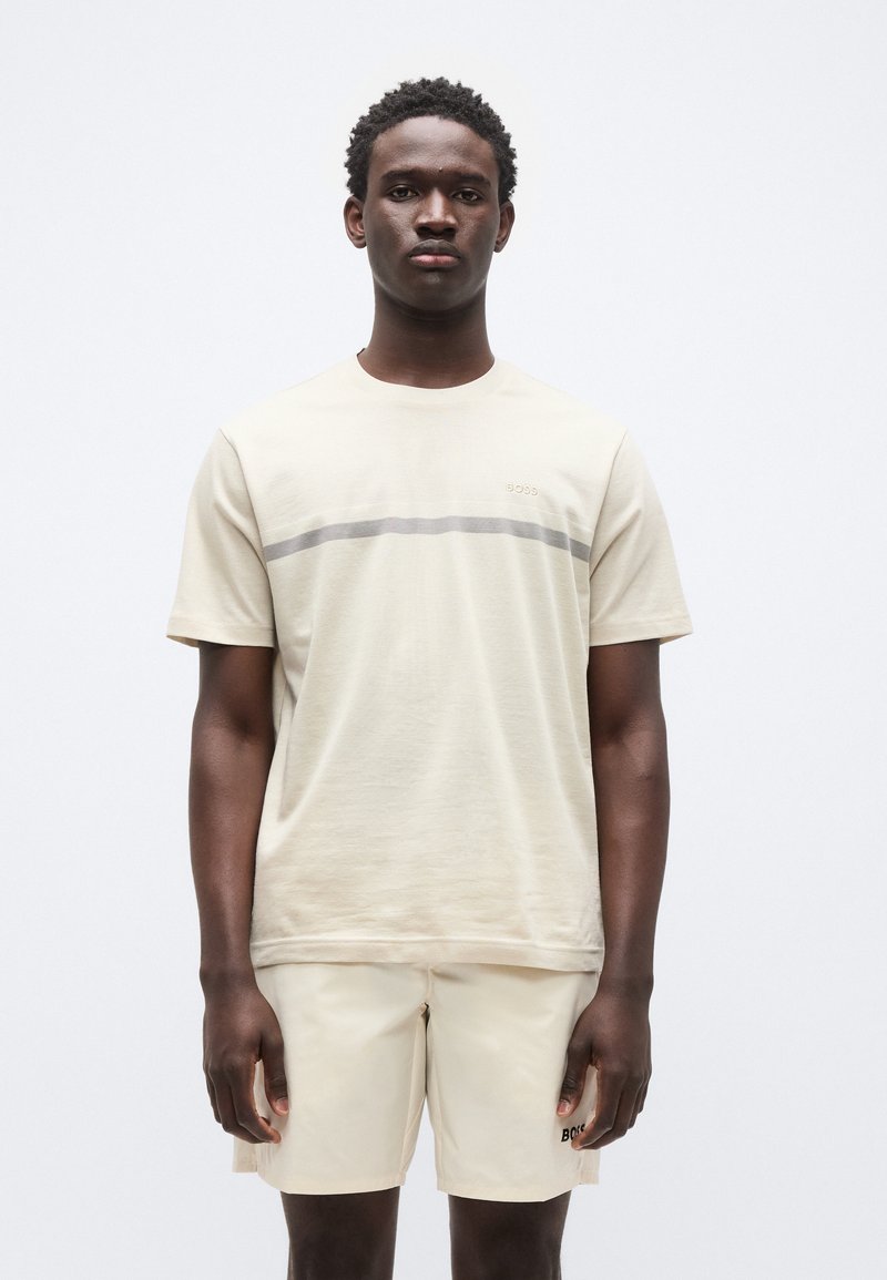 Μπεζ κοντομάνικο t-shirt με γκρι οριζόντια ρίγα στο στήθος, σετ με ταιριαστό μπεζ σορτς. Το ύφασμα φαίνεται λείο και ελαφρύ.