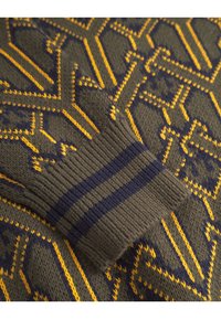 Maglione lavorato a maglia in verde oliva con un motivo geometrico giallo e blu navy, caratterizzato da polsini a costine con strisce blu e navy per aggiungere texture.