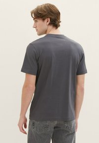 Grå bomulds T-shirt med rund halsudskæring, korte ærmer og en glat overflade, sammen med mørk denim jeans med ryglomme sømdetaljer.