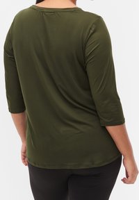 Camicia verde oliva a maniche tre quarti con scollatura rotonda, realizzata in tessuto morbido, caratterizzata da un orlo curvo e dettagli di cucitura sottili.