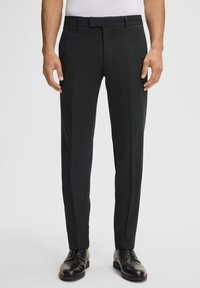 Zwarte op maat gemaakte broeken met een gladde textuur, voorzien van een platte voorkant, riemlussen en een slim fit ontwerp. G gedragen met zwarte schoenen.