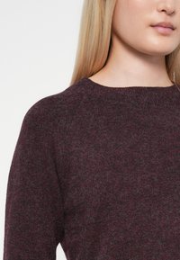 Mélykék burgundi árnyalatú kötött pulóver, kerek nyakkivágással, puha tapintással és raklanszabású ujjakra tervezve, hogy kényelmesen illeszkedjen.