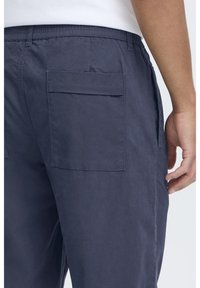 Granatowe spodnie wykonane z mieszanki bawełny, z elastycznym paskiem w talii i dużymi naszywanymi kieszeniami z tyłu. Gładka faktura i swobodny design.