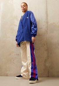 Blå dubbelknäppt kavaj med en avslappnad passform, i kombination med krämfärgade byxor med blå och röda ränder och logotyp. Svarta skor fulländar looken.
