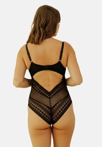 Bodysuit noir transparent avec texture à pois, accents en dentelle et découpe en V dans le dos ; bretelles ajustables et détails de garniture décoratifs.