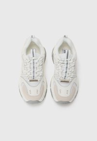 Baskets blanches et beiges avec des panneaux en mesh texturé et en cuir, présentant des accents gris et des détails réfléchissants sur les lacets et la languette.