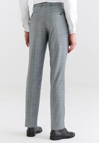 Szare spodnie w kratę o dopasowanym kroju, z dwoma tylnymi kieszeniami i gładką fakturą. Zestawione z czarnymi butami.