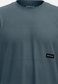 Dark blue t-shirt made of soft fabric with a crew neckline, featuring a horizontal seam and a black rectangular Ortovox logo patch.
