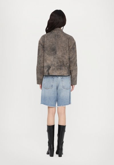 Brun texturerad jacka med krage, ihop med ljusblå denimshorts med fransar och två bakfickor. Svarta knähöga stövlar.