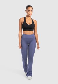 Schwarzer gerippter Sport-BH und hoch taillierte lilafarbene ausgestellte Leggings. Die Leggings haben eine glatte Textur mit einem dezenten Glanz. Enganpassendes sportliches Design.