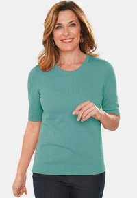 Mintgrüner Kurzarmpullover mit Rundhalsausschnitt, gerippten Abschlüssen und Saum. Weiche Textur, figurbetonter Schnitt. Getragen mit dunklen Jeans.