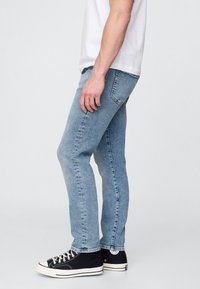 Világoskék farmernadrág szűk fazonban és enyhén kifakult hatással, fekete magas szárú tornacipőkkel párosítva, amelyek fehér díszítésekkel és fűzőkkel rendelkeznek.