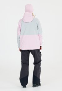 Lättvikts snöjacka i rosa och grå med huva, kombinerad med mörkgrå snöbyxor. Har en lös passform och ett slitstarkt material.