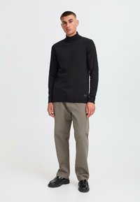 Pulover negru cu guler înalt dintr-un material tricotat fin, asortat cu pantaloni gri deschis și pantofi negri. Design simplu, siluetă ajustată.