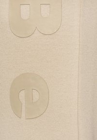 Beige Textil mit Strickstruktur, das große, hellfarbige, ausgeschnittene Buchstaben "b" und "d" deutlich zur Schau stellt.