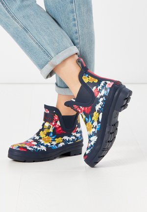 Bottes en caoutchouc à hauteur de cheville de couleur marine, avec un imprimé floral multicolore comprenant des fleurs jaunes, rouges et blanches, semelle texturée et languette pour les enfiler.