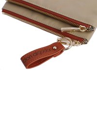 Funda de nailon beige con dos cremalleras en tono dorado, acentos rojos y una correa de cuero marrón. Presenta el nombre de la marca impreso en la correa.