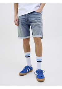 Shorts di denim di colore blu chiaro con orli risvoltati, abbinati a calzini bianchi con strisce blu e sneakers blu con suole in gomma.