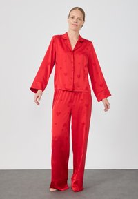 Set da pigiama in satin rosso con motivo a cuori, composto da una camicia con colletto e bottoni e pantaloni lunghi larghi con ampie pince.