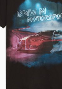 Rød og hvid BMW M racerbil, der drifter på en bane, med farverig blå og pink røg i baggrunden og teksten "BMW M Motorsport" ovenfor.