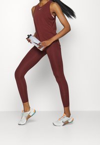 Burgundy athletic tank top and leggings paired with white and orange sneakers. The tank has a round neckline; leggings are form-fitting.