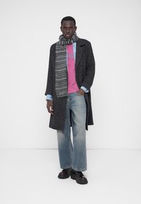 Sardi kalas herringbone-mustriga hall mantel roosa dressipluusi, teksasärgi ja laia sinise teksapükstega. Viimistletud triibulise halli salli ja mustade saabastega.