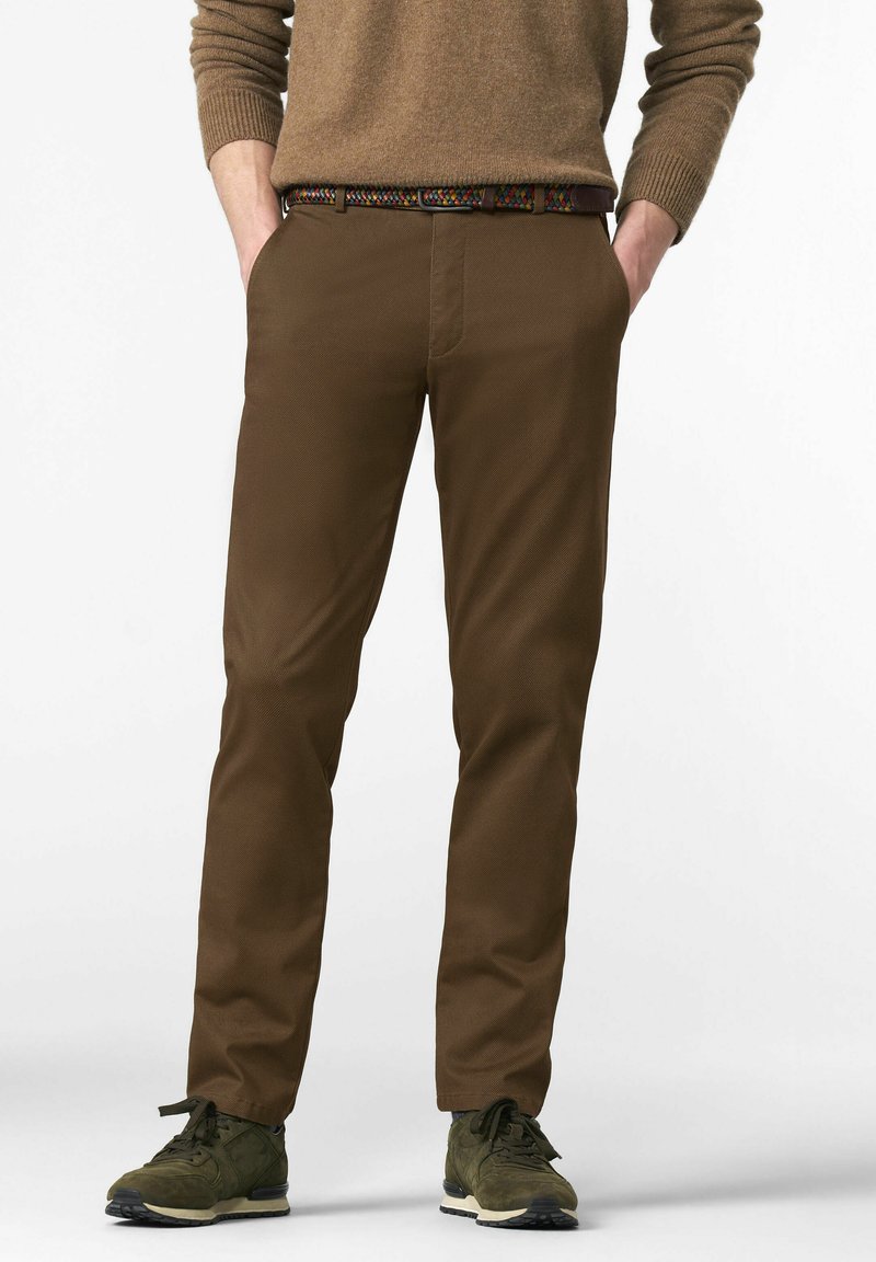 Chinos marron avec une finition texturée, dotés de poches latérales, accompagnés d'une ceinture tissée multicolore et de baskets vertes.