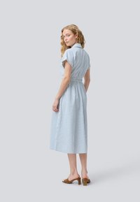 Abito a righe in azzurro chiaro e bianco, con colletto, maniche corte e vita aderente. Di lunghezza media con una gonna fluente e spacchi laterali.