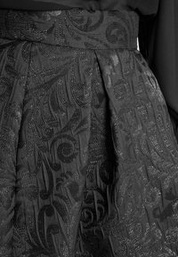 Zwarte stof met intrigerende, kronkelige bloempatronen, voorzien van glanzende, gestructureerde borduursels op een geplooid kledingstukdeel.