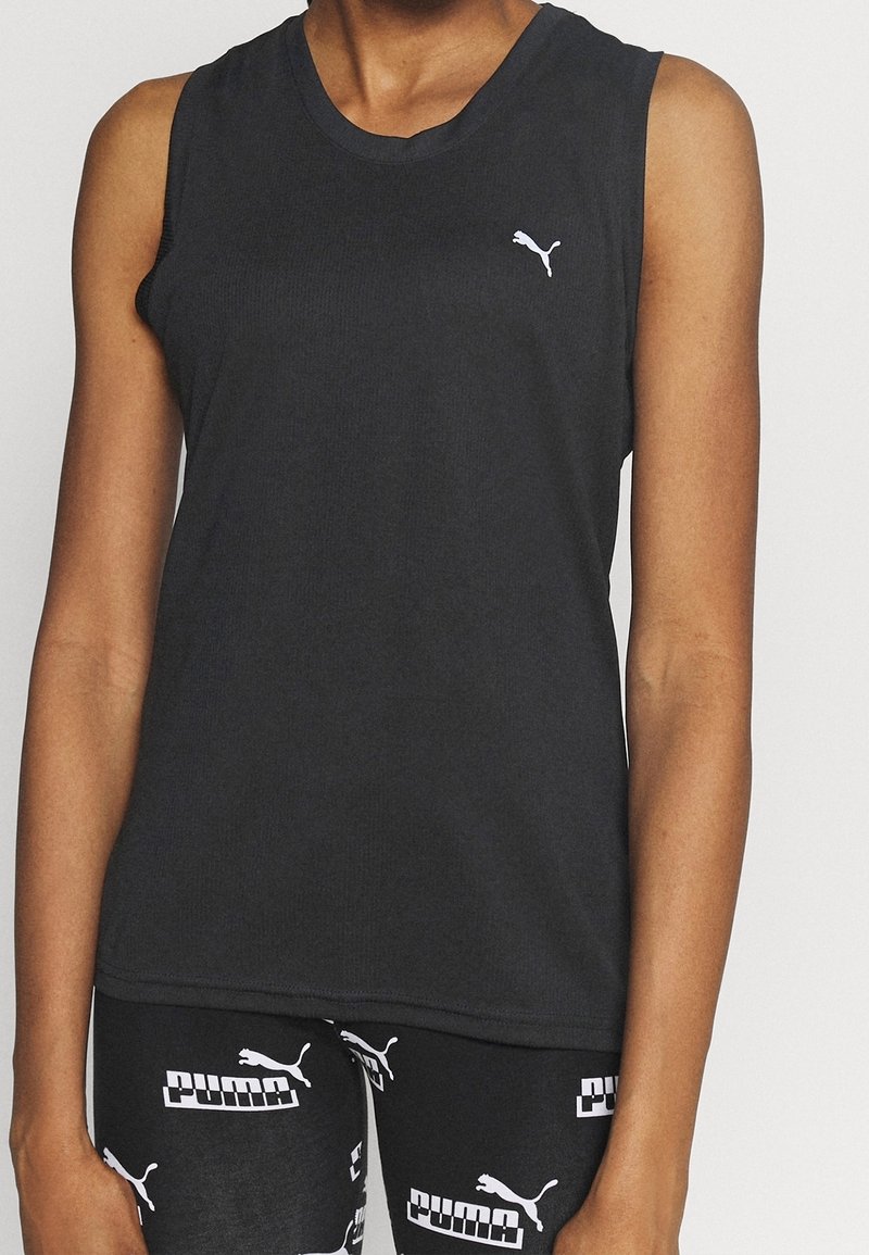 Personne portant un top sans manches noir Puma et un legging noir avec des logos blancs Puma répétés.