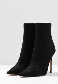 Bottes basses en daim noir avec un bout pointu, un talon aiguille et un design sans coutures. Coutures visibles le long de la couture avant.
