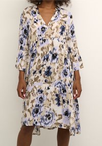 Robe florale avec une coupe ample, un décolleté en V, des manches trois-quarts, et un mélange de tons bleus, beiges et noirs dans un tissu texturé.