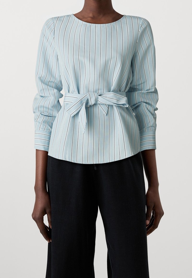 Chemisier bleu clair à col avec des rayures blanches verticales. Doté d'une taille nouée et de manches longues avec des détails froncés. Texture lisse.