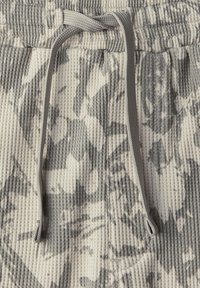 Strukturalny materiał w odcieniach beżu i szarości z wzorem, z paskiem ściągającym w talii. Posiada falisty wzór i prążkowaną strukturę z dwiema bocznymi kieszeniami.