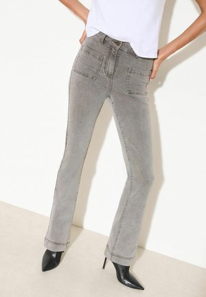 Femme portant un jean en denim gris taille haute avec des poches plaquées à l'avant et des bottes noires à talons hauts et bout pointu.