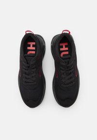 Chaussures de sport noires en tissu mesh, avec des accents rouges et un logo sur les semelles intérieures. Conçues avec une semelle texturée et un système de laçage.