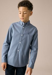 Camicia azzurro chiaro con bottoni, maniche lunghe, colletto e bottoni bianchi; presenta un logo ricamato sul petto sinistro.