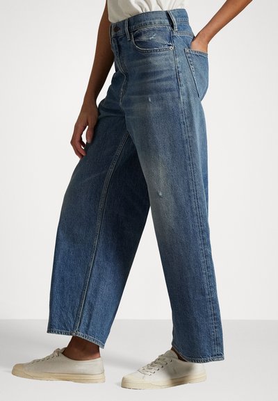 Høyt liv, løstsittende blå denimjeans med en falmet finish, sidelommer og rå skjæring, parret med lyse sneakers.