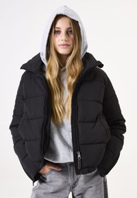 Schwarz gesteppte Daunenjacke mit hoher Kragen, getragen über einem grauen Kapuzenpullover. Verfügt über Reißverschluss und Seitentaschen. Strukturiertes Material.