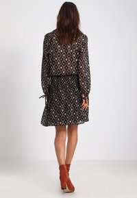 Robe noire avec des motifs en diamants beige, rose et blanc. Comprend des manches longues, une taille froncée et une jupe évasée. Modèles des bottines.