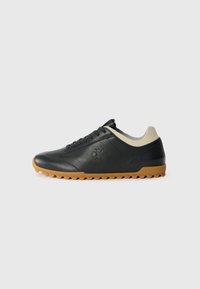 Black leather sneakers with a textured finish, featuring a cream-colored collar, lace-up design, and a gum rubber sole with traction studs.