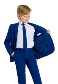 Abito blu con cravatta coordinata, camicia bianca visibile, giacca aperta che mostra la fodera interna, texture liscia, vestibilità su misura e tasche visibili.