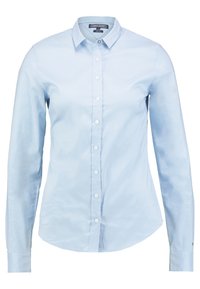 Camisa de mujer azul claro, de manga larga y corte ajustado, con un collar clásico y botones blancos en el frente.