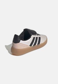 Zapatillas deportivas en blanco y negro con parte superior de cuero liso, tres franjas laterales y suela de goma color cuero. Cuenta con lengüeta y talón acolchados.