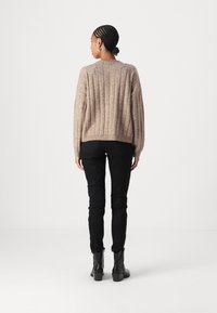 Beige bordázott pulóver, laza fazonnal, kerek nyakú és hosszú ujjú, fekete, slim fit nadrággal és bokacsizmával párosítva.