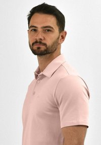 Polo shirt in zacht roze, korte mouwen, met een knoopsluiting van drie knopen, ronde kraag, gladde textuur, met een subtiele logodetail op de borst.
