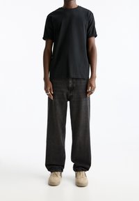 T-shirt nera a maniche corte abbinata a jeans grigia scura a vestibilità comoda e sneakers beige, caratterizzata da un design semplice e una vestibilità rilassata.
