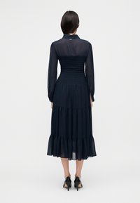 Μακρυμάνικο φόρεμα σε ναυτικό μπλε χρώμα με σφηκοφωλιά κορσέ, πολυεπίπεδη φούστα και γιακά. Διαφανές ύφασμα πάνω από τη μέση που τονίζει τη μέση.