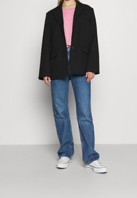 Blazer negro de corte Oversize con un solo botón, llevado sobre un top rosa, combinado con unos jeans de pierna recta azul claro y zapatillas blancas.